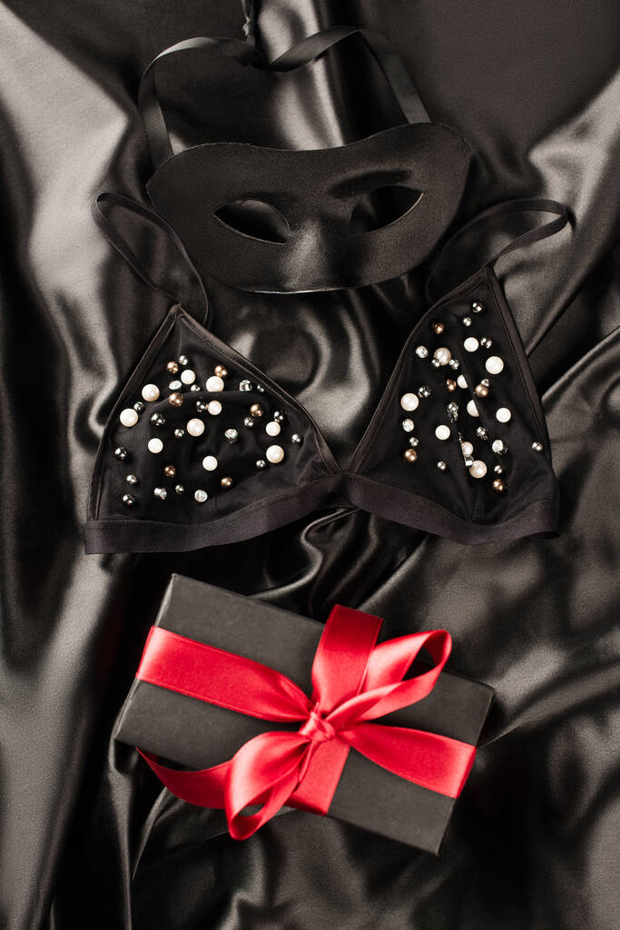 Siyah saten arka planda sütyen ve cinsel maskenin yanında mevcut görünümün üst görüntüsü - Fotoğraf, Görsel