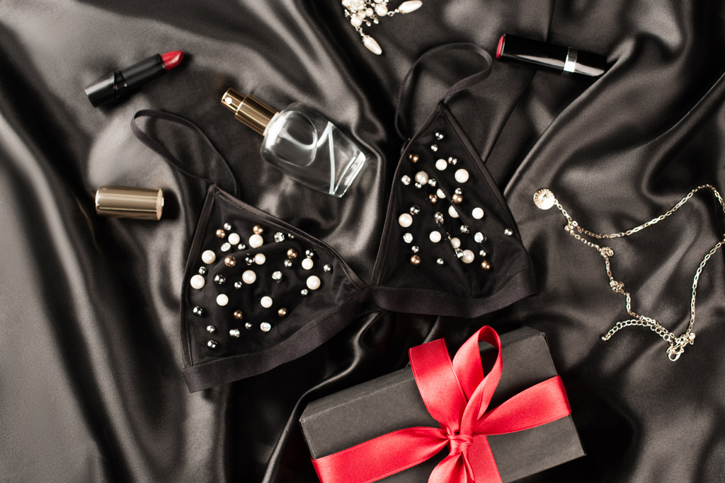 Вид зверху бюстгальтер, подарунок і парфуми біля губ на чорному атласному фоні
 - Фото, зображення