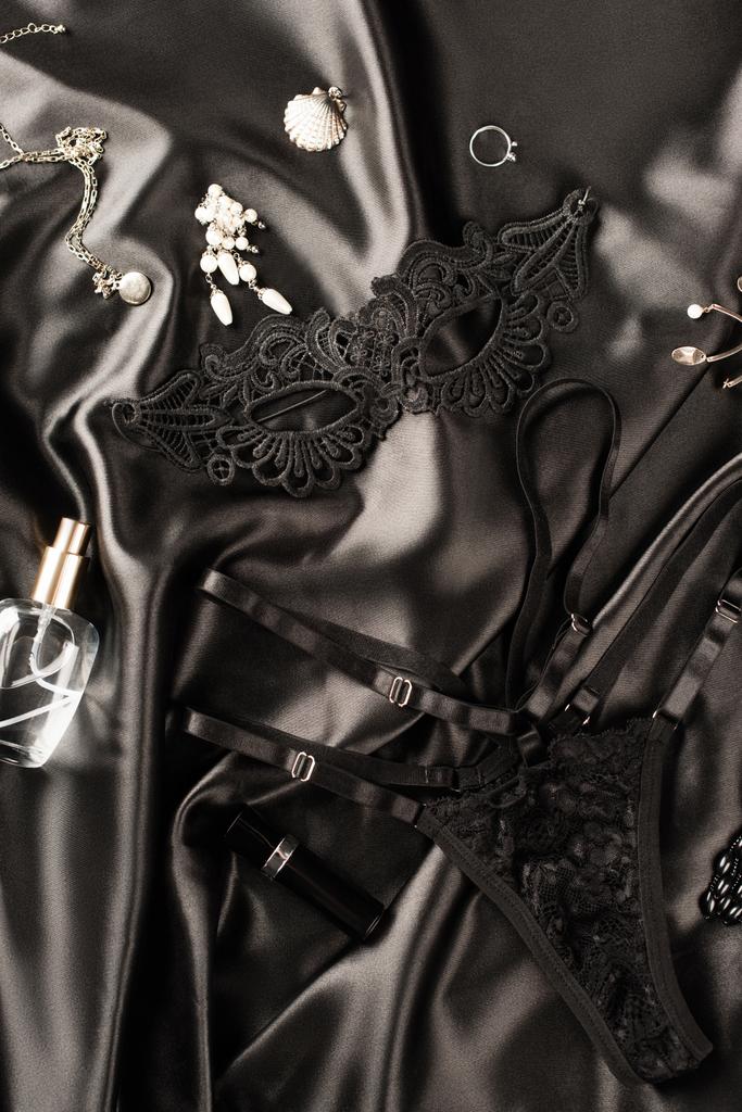 Vista superior de la máscara sexual, bragas y perfume sobre fondo satinado negro - Foto, Imagen