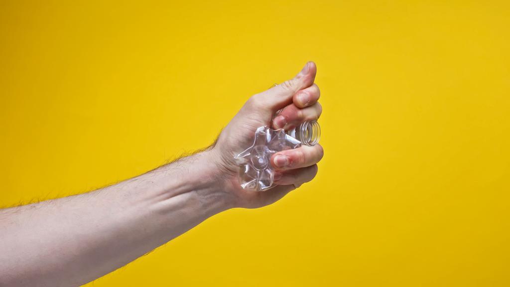 καλλιεργημένη άποψη του ανθρώπου θρυμματίζοντας πλαστικό μπουκάλι απομονωμένο σε κίτρινο, μηδενική έννοια αποβλήτων  - Φωτογραφία, εικόνα