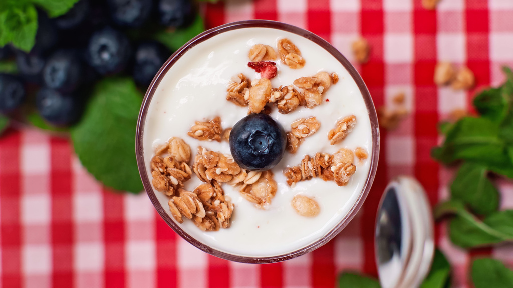 bovenaanzicht van bosbes en granola bovenop verse yoghurt in glas  - Foto, afbeelding