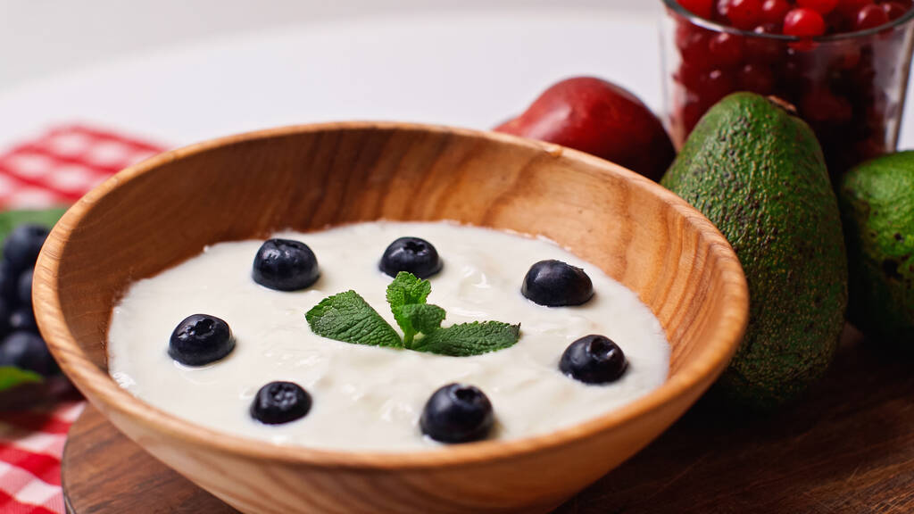 świeże owoce w pobliżu drewnianej miski z jogurtem i jagodami na białym - Zdjęcie, obraz