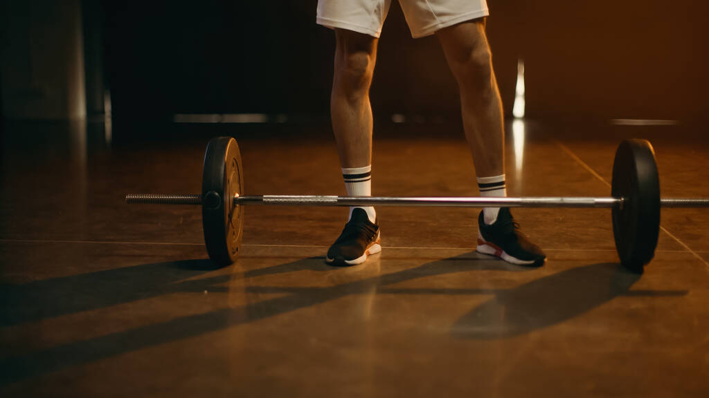 Обрізаний вид спортсмена, що стоїть біля барбелла на темному тлі
 - Фото, зображення