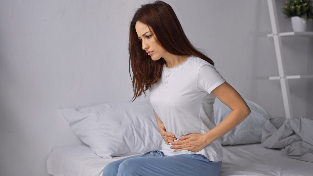brunetka žena dotýkání břicha, zatímco pocit bolesti břicha v ložnici - Fotografie, Obrázek