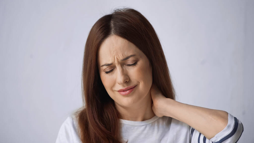 kobieta z zamkniętymi oczami marszczenie brwi podczas odczuwania bólu w szyi na szarym tle - Zdjęcie, obraz