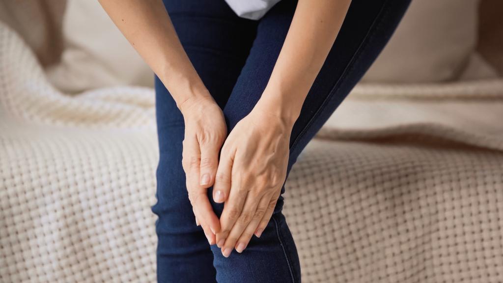 oříznutý pohled na ženu dotýkající se bolestivého kolena, když stojí doma - Fotografie, Obrázek