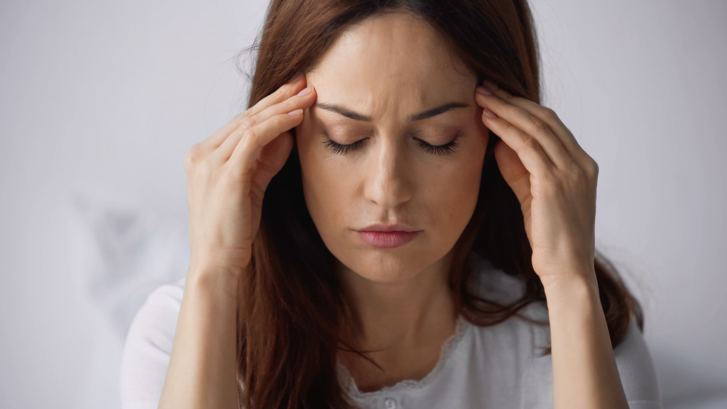 brünette Frau mit geschlossenen Augen, die Kopf berührt, während sie an Migräne auf grauem Hintergrund leidet - Foto, Bild