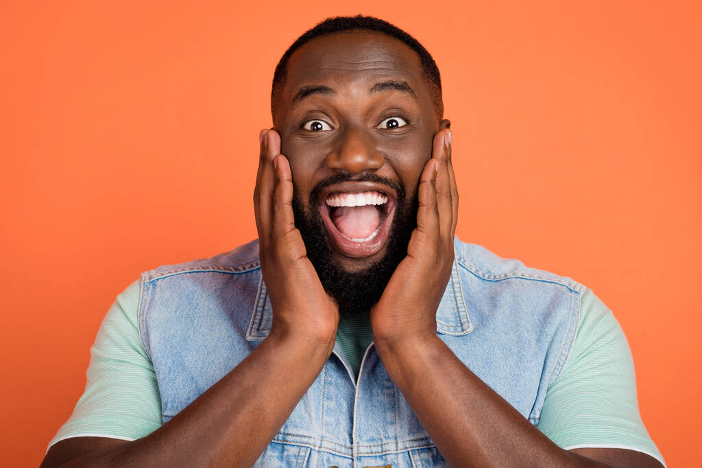 Fotografie šokované roztomilé afro chlap nosit džínové vesty tváře otevřené ústa izolované oranžové barvy pozadí. - Fotografie, Obrázek