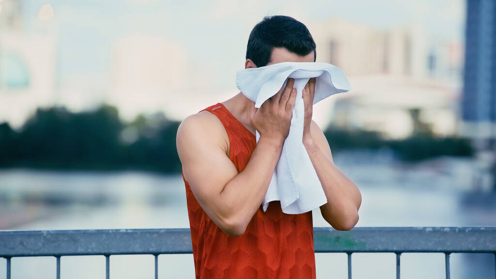 joven deportista limpiando la cara con toalla mientras está de pie en el puente - Foto, imagen