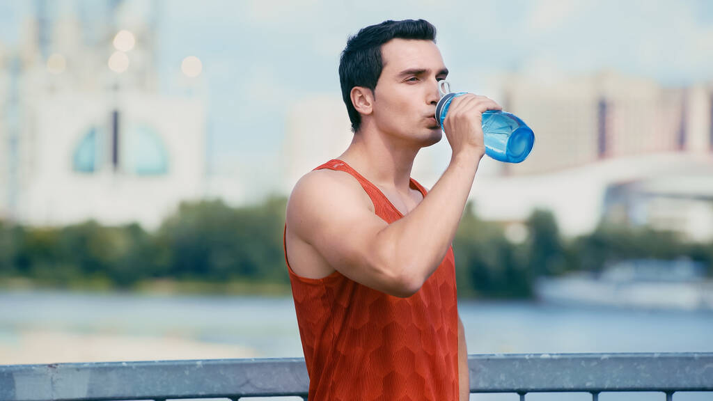 joven deportista de pie en el puente y beber agua de la botella de deportes
 - Foto, Imagen
