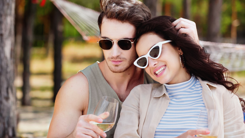 Férfi napszemüvegben megérinti a mosolygó barátnő haját borral a strandon  - Fotó, kép
