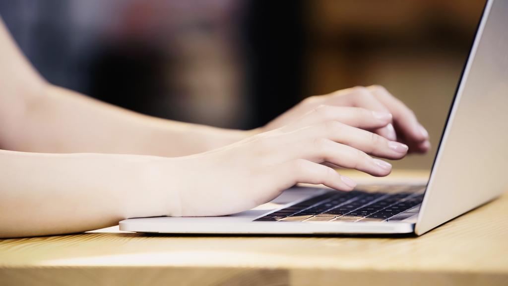 καλλιεργημένη άποψη της νεαρής γυναίκας δακτυλογράφηση σε φορητό υπολογιστή στο καφέ  - Φωτογραφία, εικόνα