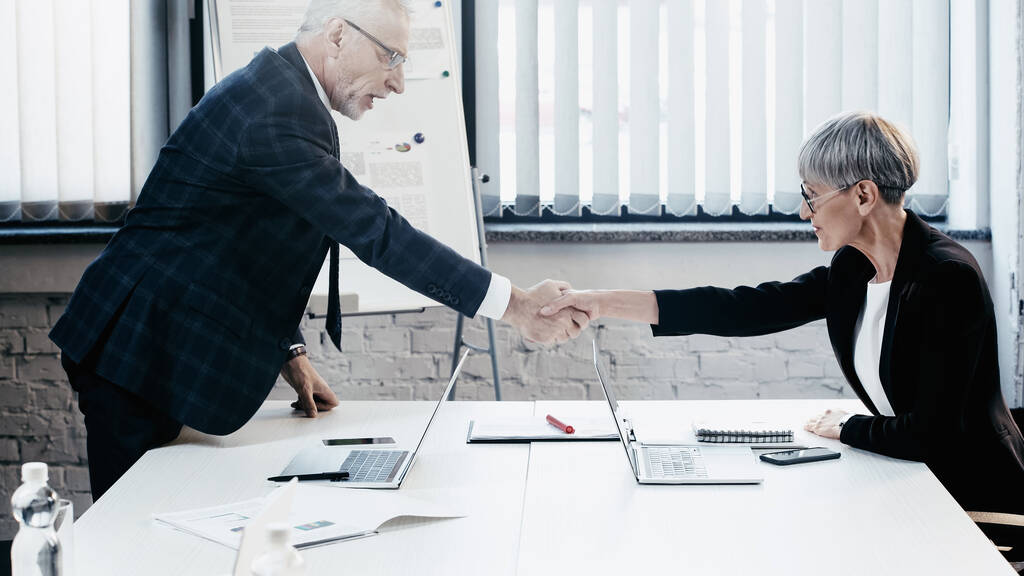 Вид збоку середнього віку бізнесмени тремтять руками біля гаджетів і паперів в офісі
  - Фото, зображення