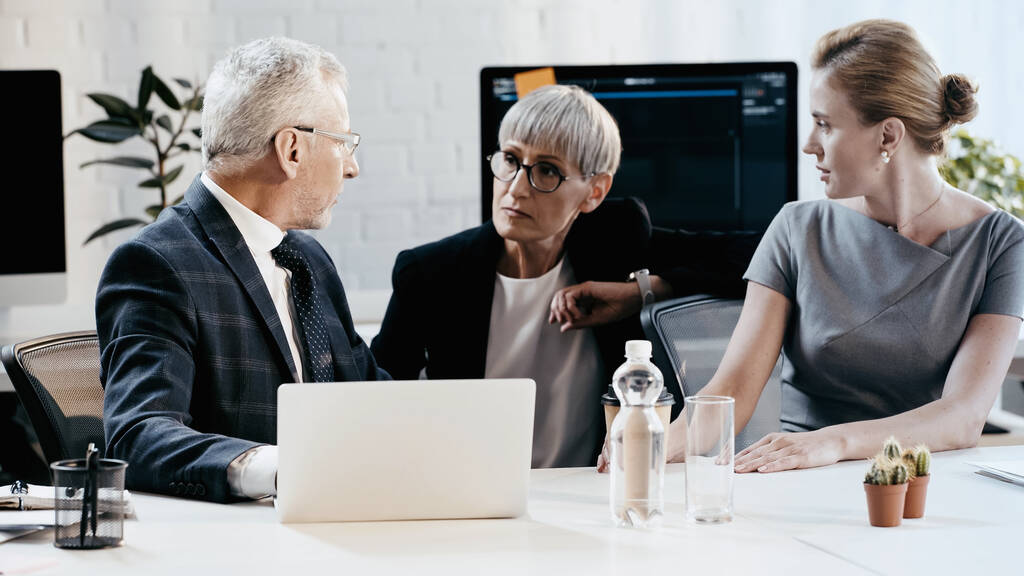 Empresários em uso formal conversando perto de laptop e papéis no escritório  - Foto, Imagem