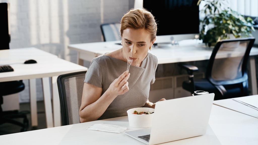 Üzletasszony eszik friss salátát kávé mellett menni, és laptop az irodában  - Fotó, kép