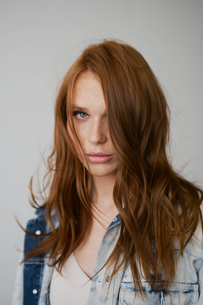 赤い髪、青い目と長い波状の赤い髪を持つ素敵なモデル。官能的な魅力的な女性。そばかす。中立的背景。優れた品質。柔らかい光だ。ジーンズジャケット。素敵なまつ毛、大きな唇、美しい目 - 写真・画像