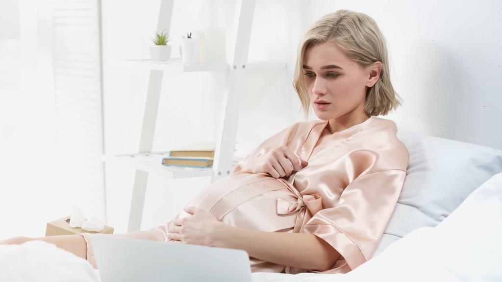 сумна блондинка вагітна жінка дивиться фільм на ноутбук у спальні
  - Фото, зображення