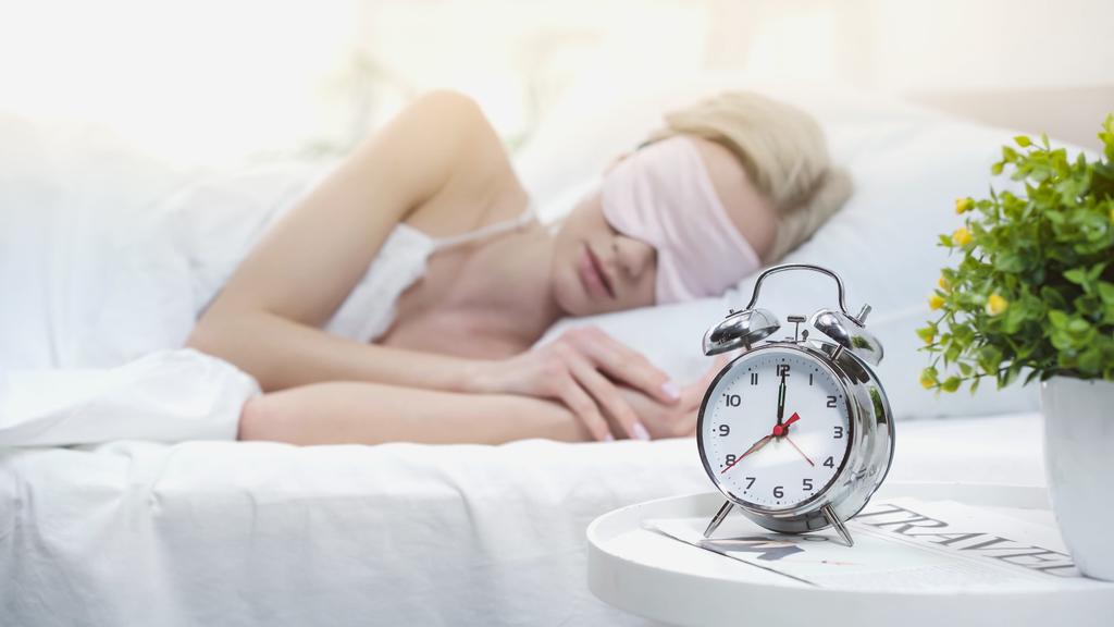 jong blond vrouw in slaap masker liggend in bed - Foto, afbeelding