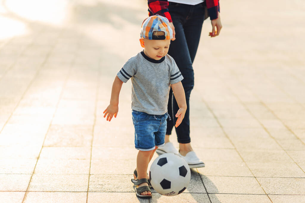 Anya és fia együtt fociznak a parkban, a kisfiú focilabdázik, a gyerek focizni tanul. A család együtt focizik a parkban. - Fotó, kép