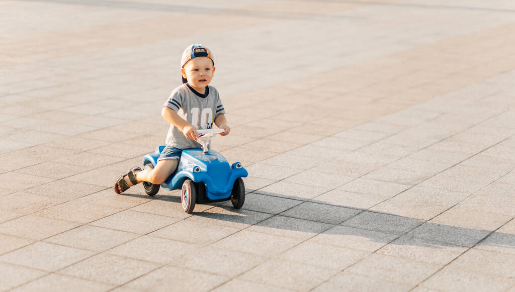 Kleiner Junge fährt auf einem Spielzeugauto im Park, glückliches Kind an einem sonnigen Sommertag, Auto fahren im Freien. Das Konzept der Kindheit, Unterhaltung, Outdoor-Aktivitäten mit Kindern an einem warmen Sommertag. - Foto, Bild