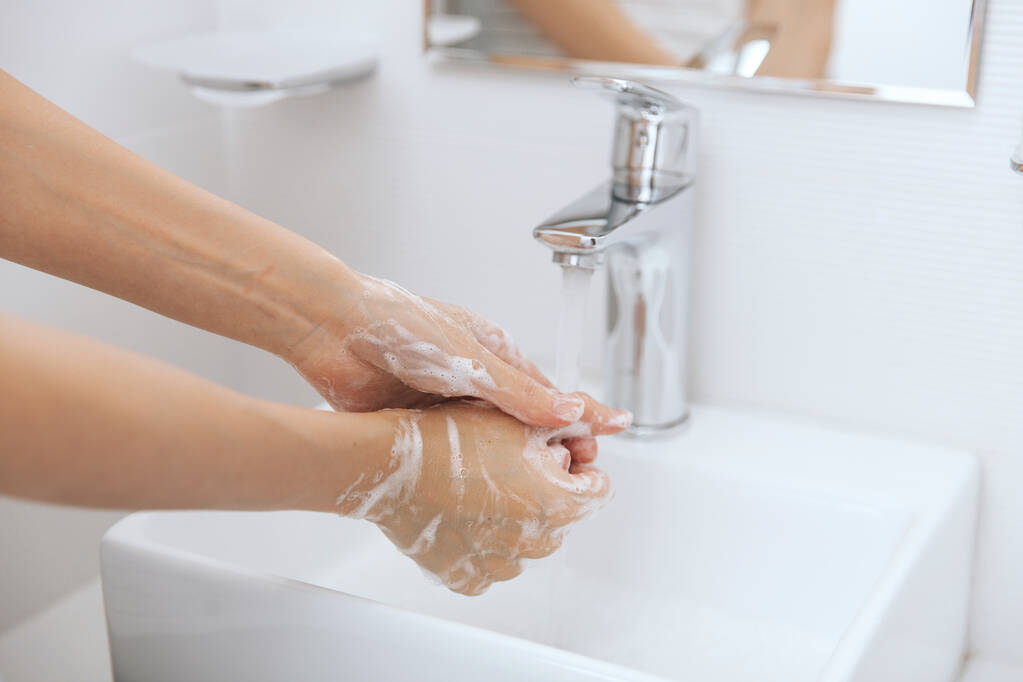 Hände waschen unter dem fließenden Wasserhahn. Händewaschen mit Seife zur Vorbeugung des Coronavirus, Hygiene gegen die Ausbreitung des Coronavirus in öffentlichen Waschräumen. Hygienekonzept Hand in Hand - Foto, Bild