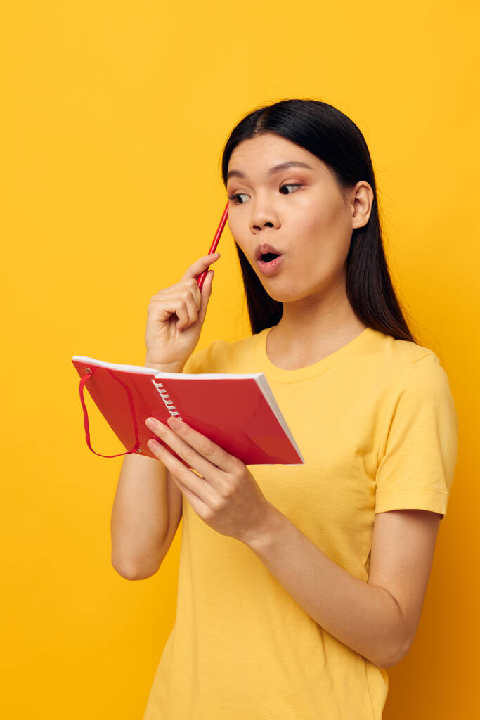 Charmant jong aziatisch vrouw in een geel t-shirt rood notebook opleiding studio model ongewijzigd - Foto, afbeelding