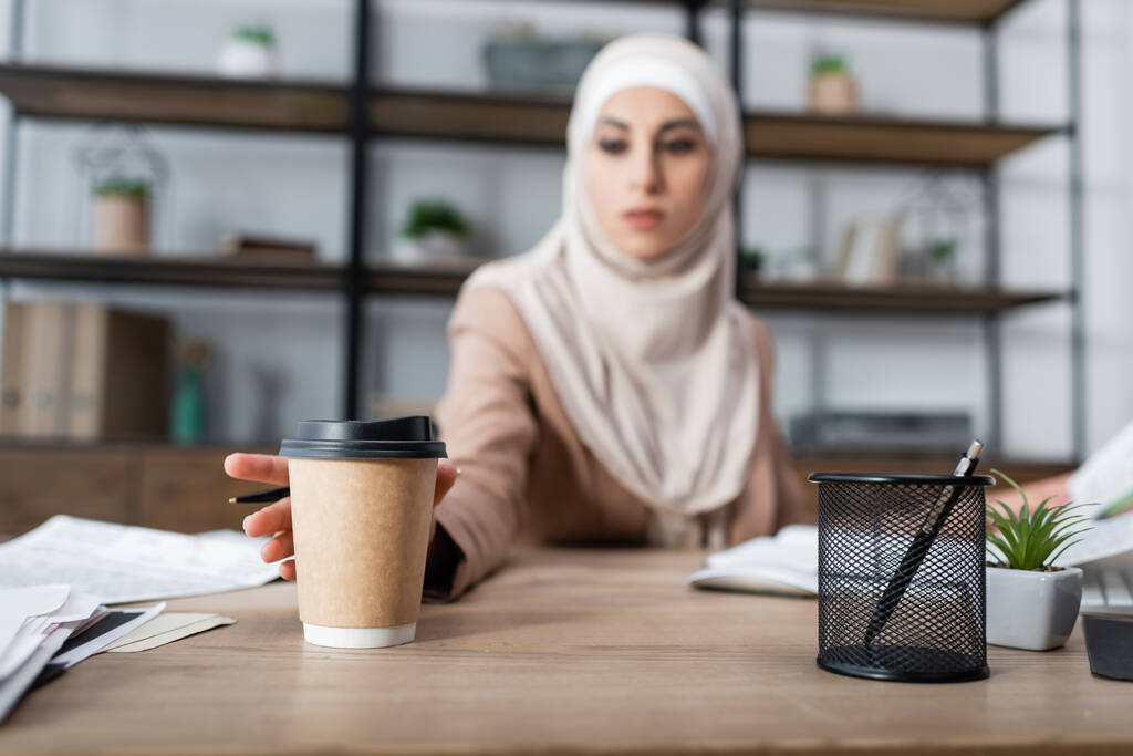 mulher árabe borrada atingindo copo de papel enquanto trabalhava em casa  - Foto, Imagem