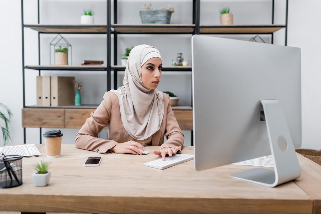 młoda muzułmanka pracuje na komputerze w pobliżu smartfona z pustym ekranem i kawą na wynos - Zdjęcie, obraz