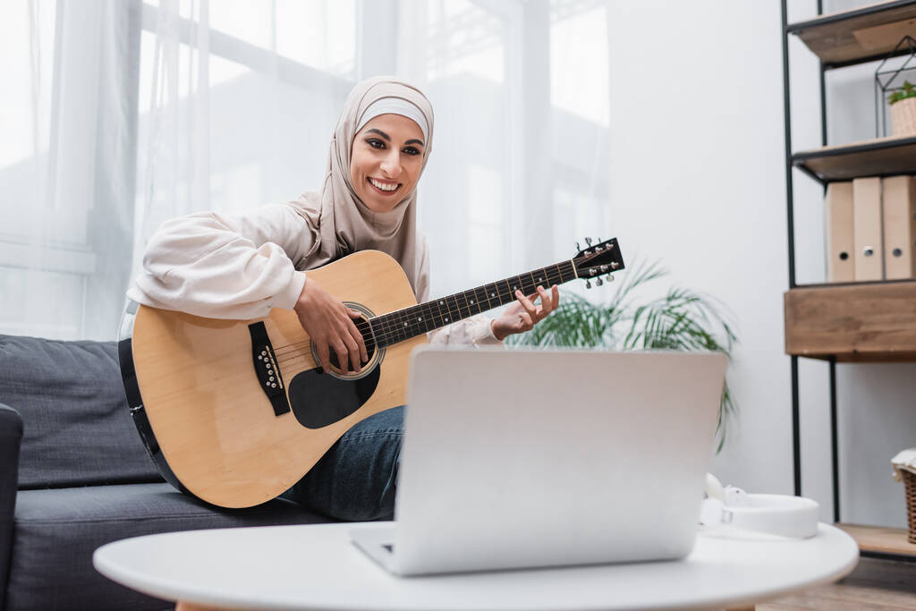 明るいアラビア人女性は家でギターを習いながらぼやけたノートパソコンを見て - 写真・画像