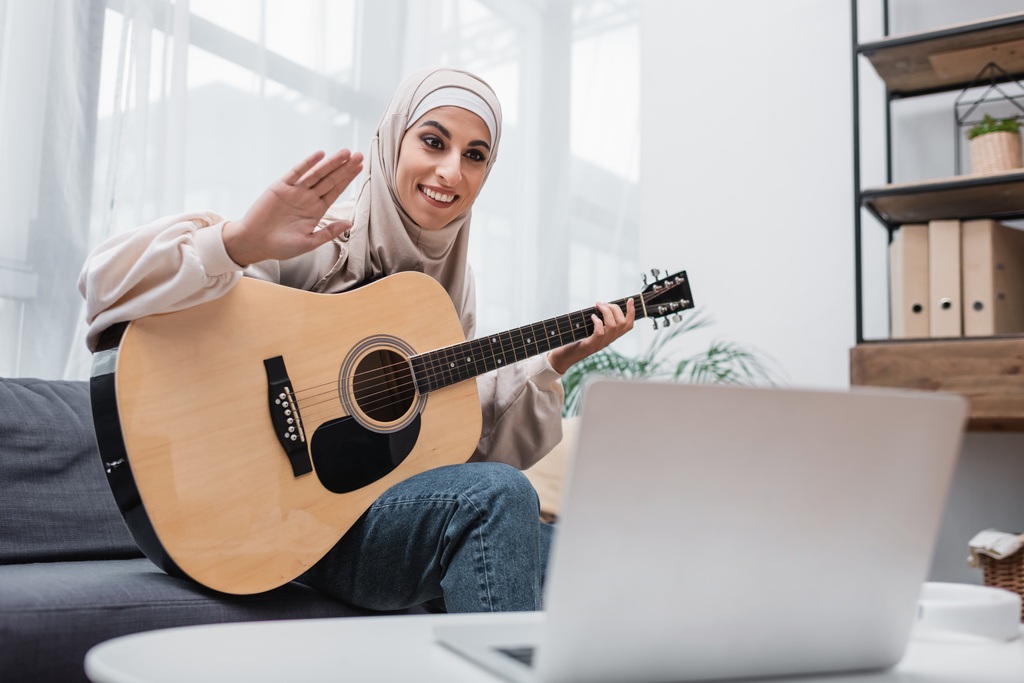 heureuse femme musulmane agitant la main pendant la leçon de guitare en ligne - Photo, image