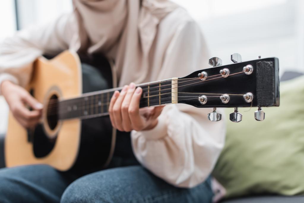 oříznutý pohled rozmazané ženy hrající na kytaru, když sedí doma - Fotografie, Obrázek