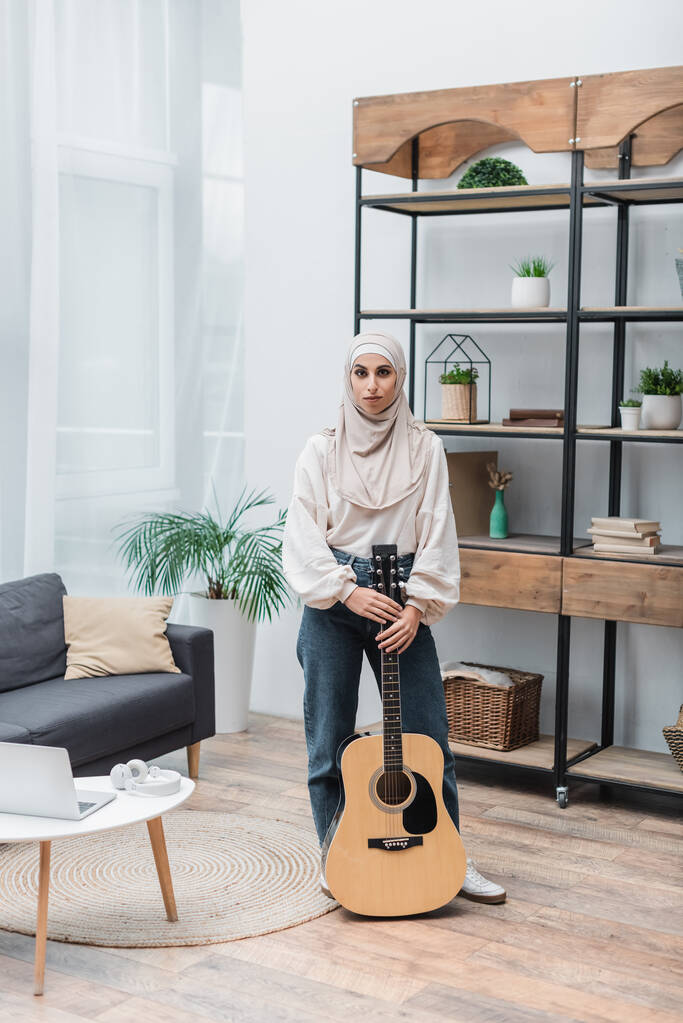 άποψη πλήρους μήκους της γυναίκας μουσουλμάνων με ακουστική κιθάρα στο σαλόνι - Φωτογραφία, εικόνα
