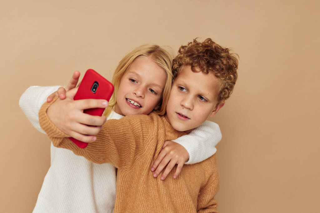 Fénykép két gyermek pulóverben pózol szórakozásból telefon elszigetelt háttér - Fotó, kép