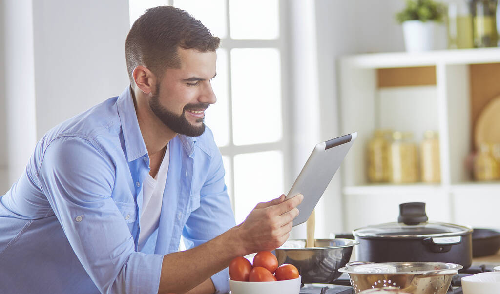 デジタルタブレット上のレシピに従う男と自宅でキッチンでおいしいと健康食品を調理 - 写真・画像
