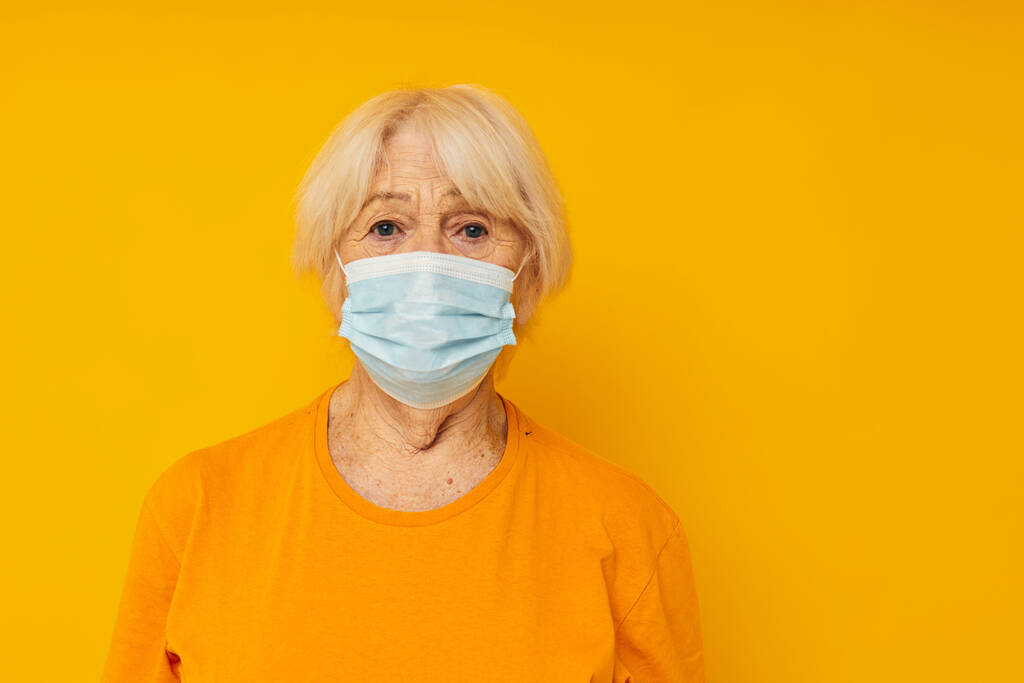Fénykép nyugdíjas idős hölgy sárga pólóban orvosi maszkok sárga háttér - Fotó, kép
