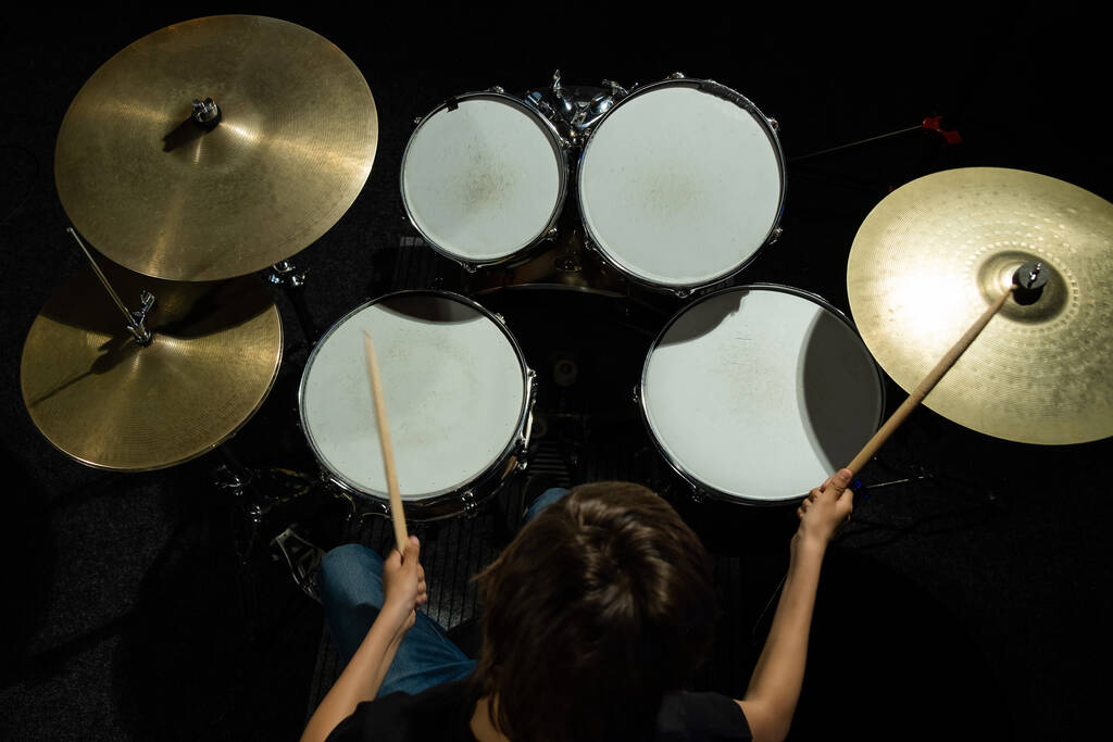 Vista superior de un niño aprendiendo a tocar la batería en el estudio sobre un fondo negro. Un estudiante de una escuela de música. - Foto, imagen
