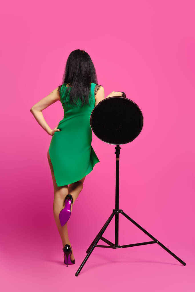 Takana näkymä nainen mustat hiukset ja vihreä mekko nousee yksi jalka ja nojaten studio strobe - Valokuva, kuva