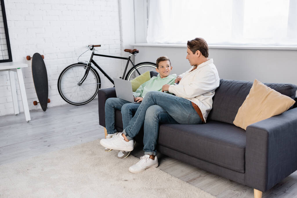 Positive kid using laptop near father on couch  - Photo, Image