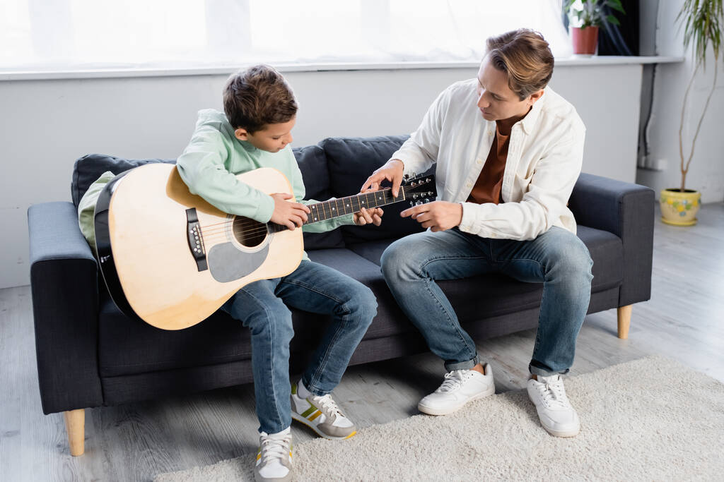 Père enseignant fils avec guitare acoustique à la maison  - Photo, image