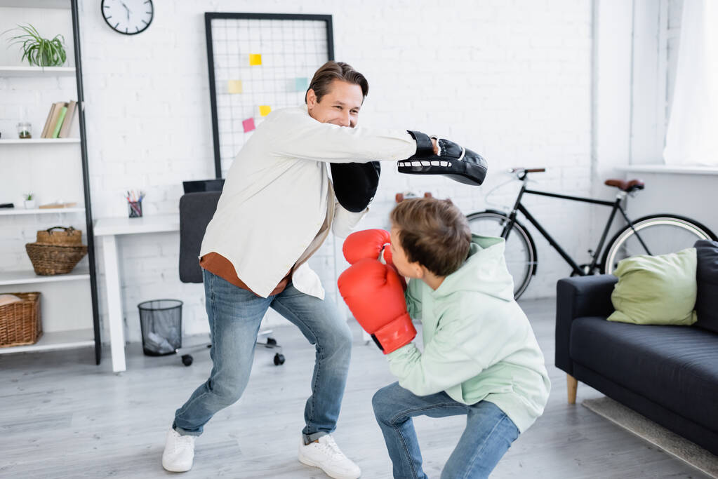 Папа и сын-подросток в боксёрских перчатках тренируются в гостиной  - Фото, изображение