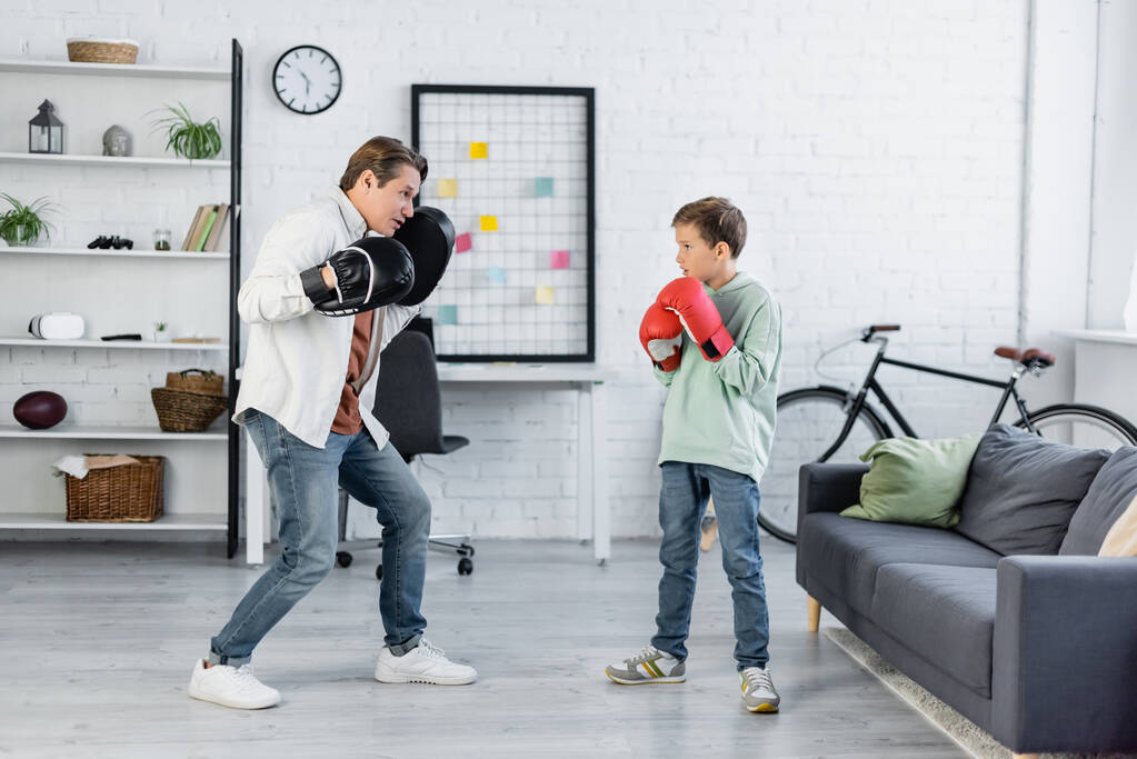 Sivukuva isästä nyrkkeilyhanskoissa katsomassa poikaa nyrkkeilyhanskoissa kotona  - Valokuva, kuva