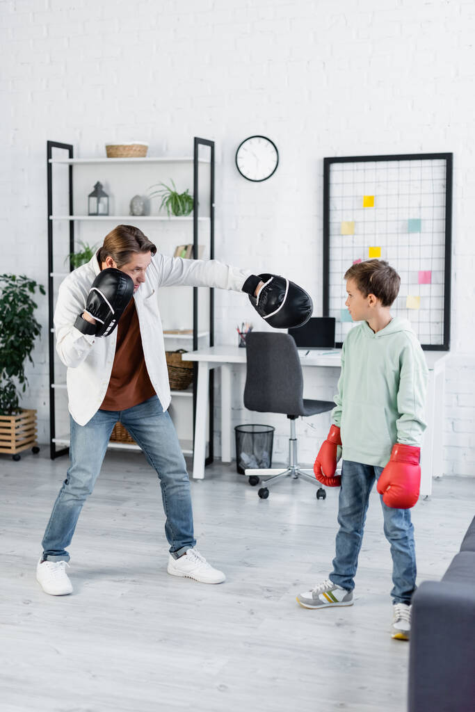 Άντρας σε punching pads διδασκαλία γιο σε γάντια πυγμαχίας στο σπίτι  - Φωτογραφία, εικόνα