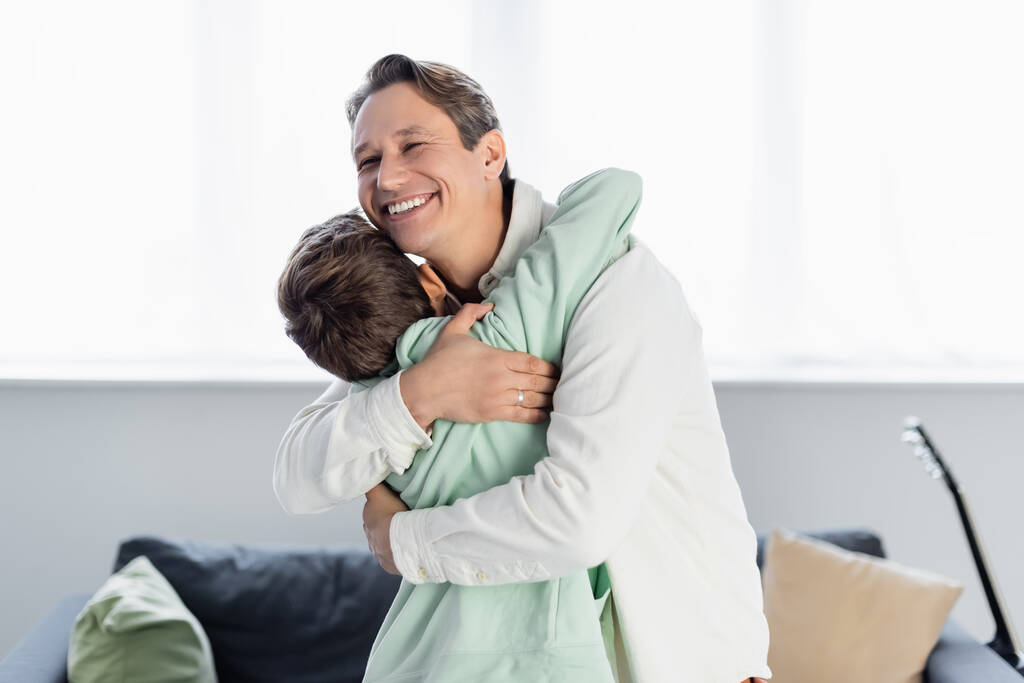 Mann umarmt vorpubertären Sohn im Wohnzimmer  - Foto, Bild