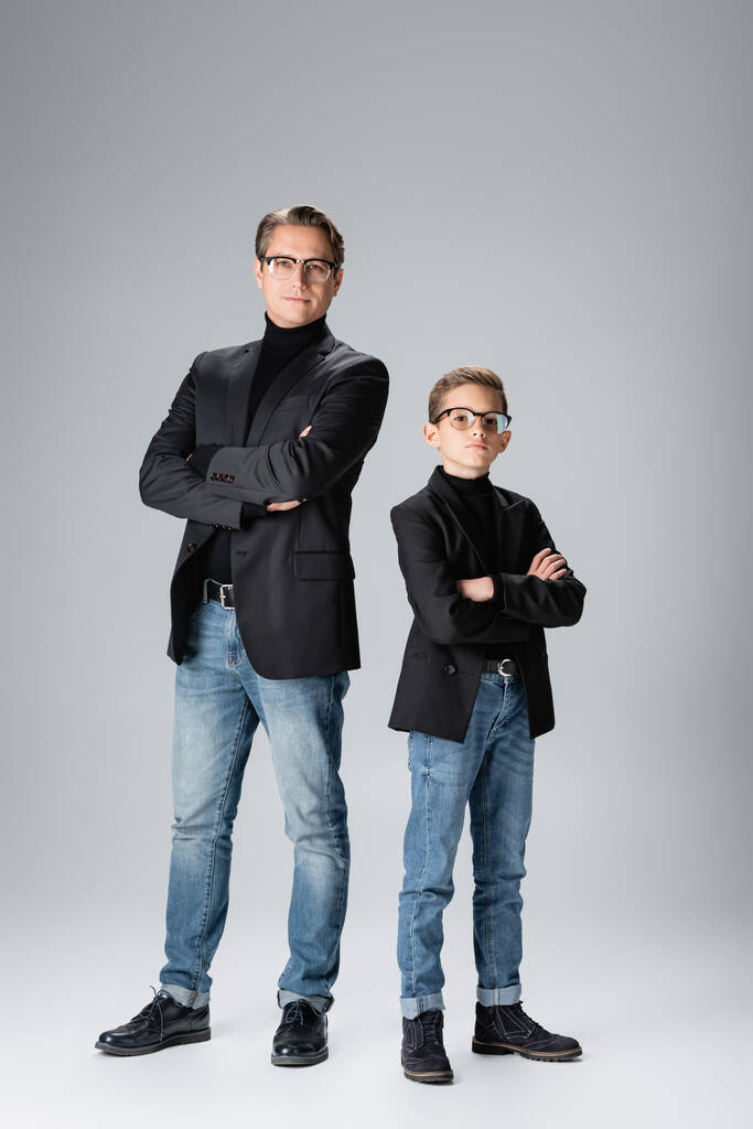 Vater und Sohn in Jacken, die sich vor grauem Hintergrund die Arme verschränken  - Foto, Bild
