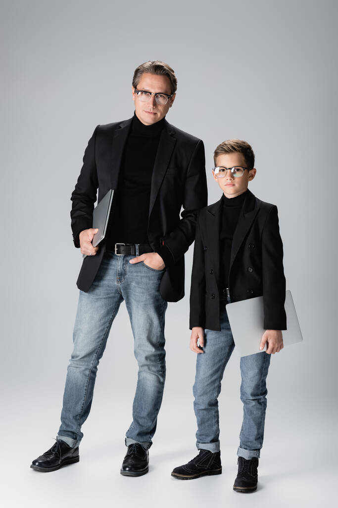 Стильний батько і син тримають ноутбуки на сірому фоні
  - Фото, зображення