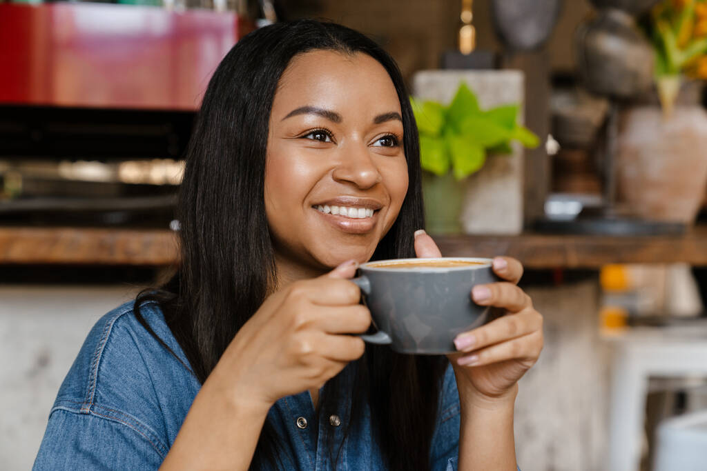 Закрыть портрет красивой африканской американки, улыбающейся с чашкой кофе в помещении - Фото, изображение