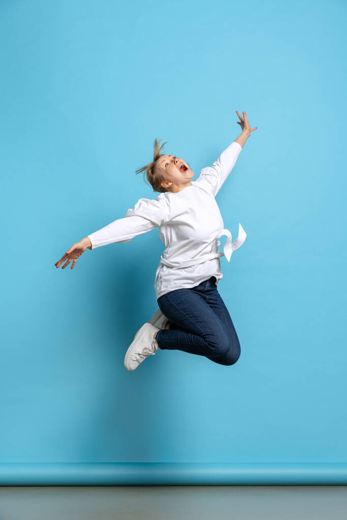 Ολόσωμο πορτραίτο ενθουσιασμένου κοριτσιού που πηδάει απομονωμένο σε μπλε φόντο. Έννοια των συναισθημάτων wow, εκφράσεις του προσώπου, διαφήμιση, πωλήσεις - Φωτογραφία, εικόνα
