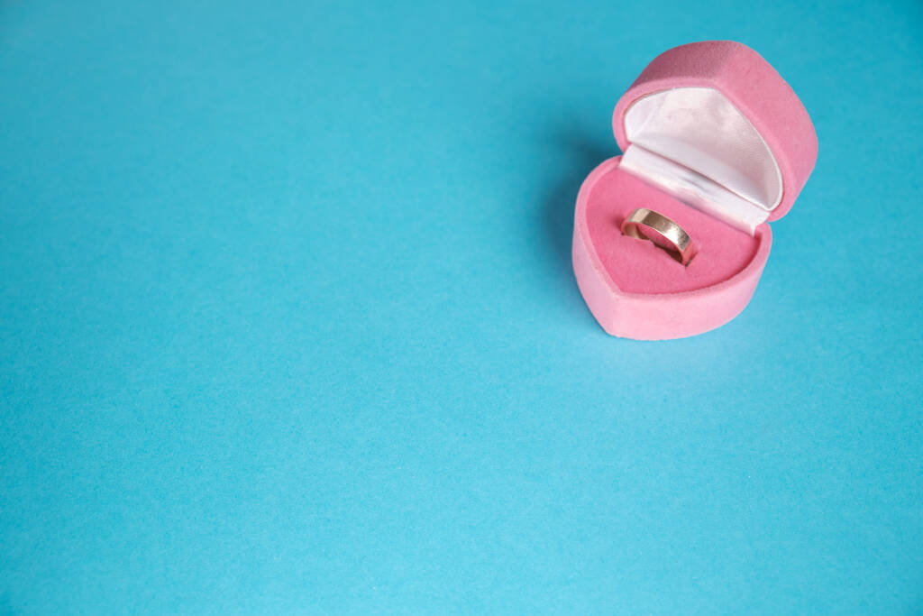 Anillo de compromiso de joyería de oro en caja rosa en forma de corazón sobre fondo azul hermoso plano. Concepto de regalo, alegría, felicidad, familia, amor, día de San Valentín. - Foto, imagen