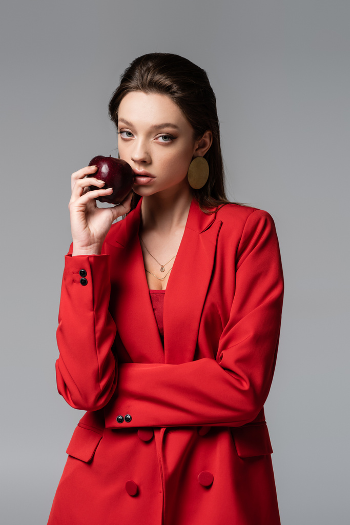灰色に隔離されたリンゴを持った赤いスーツの若い女性  - 写真・画像