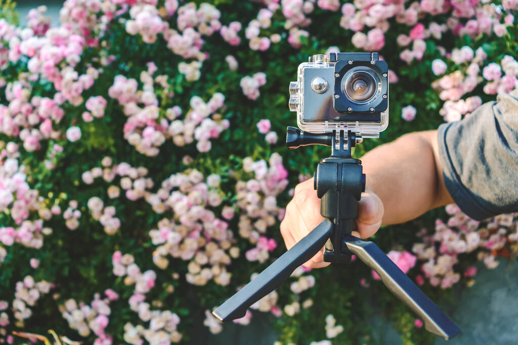 Close-up, câmera de ação na mão de um homem. Contra o pano de fundo de rosas rosa crescente - Foto, Imagem
